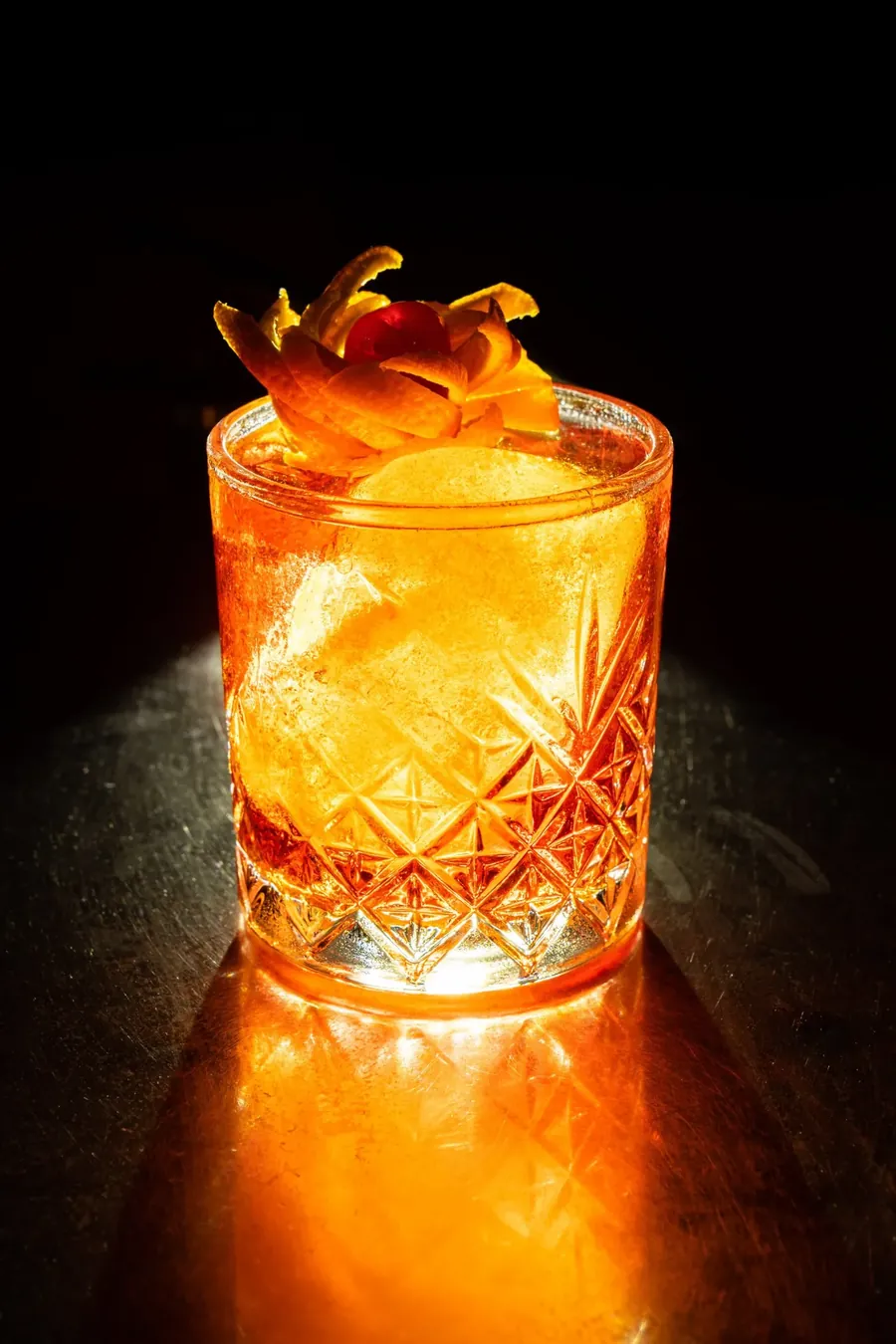 An Old Fashioned with an orange-peel rose, glowing in low light