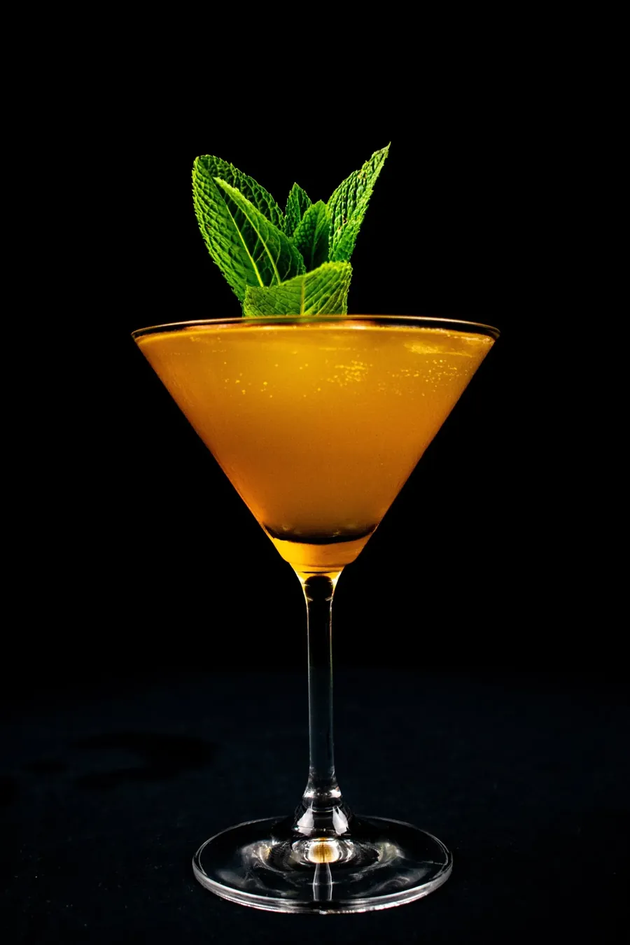 A golden cocktail in a martini glass, garnished with mint